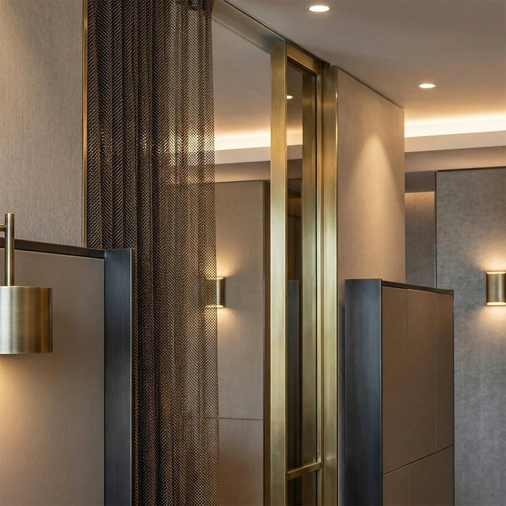 Close‑up of contemporary luxury interior detailing with metal mesh curtains and polished brass finishes against neutral surfaces.